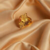 "Divy Gold 1 Gram Gold-Plated Ornate Floral Shield Ring displayed on soft beige satin fabric – ethnic elegance for every occasion."